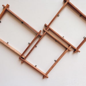 May include: Three wooden picture frames are mounted on a white wall. The frames are arranged in a staggered pattern, with the top frame slightly offset to the right. The frames are made of natural wood with a light brown finish. Each frame has a simple, rectangular shape and is secured to the wall with small metal hooks.