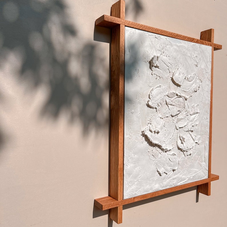 Textured white plaster artwork framed in natural wood casts shadows on a neutral wall. Available sizes include 12x16, 16x20, 18x24,24x36,30x40, and 30x48 inches, with a smooth frame extending slightly beyond the edges for a balanced, handcrafted look