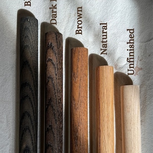This image shows five wooden dowels with different finishes. From left to right: Black (dark, sleek finish), Dark Brown (deep wood grain), Brown (classic warm tone), Natural (light, clear finish), and Unfinished (raw wood, no coating)