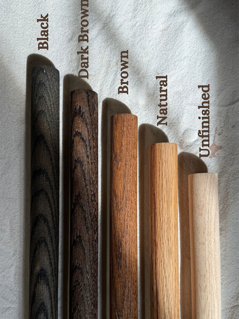 This image shows five wooden dowels with different finishes. From left to right: Black (dark, sleek finish), Dark Brown (deep wood grain), Brown (classic warm tone), Natural (light, clear finish), and Unfinished (raw wood, no coating)
