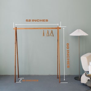 Puede incluir: Un perchero de madera con acabado natural. El perchero tiene 152,4 cm de alto, 132,1 cm de ancho y 40,6 cm de profundidad. Tiene un dise&ntilde;o sencillo con una barra horizontal y dos patas inclinadas.