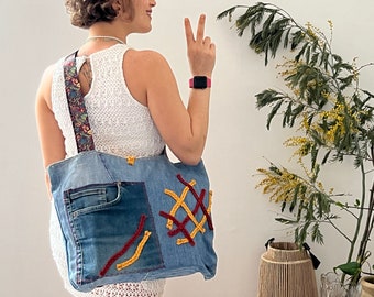 May include: A blue denim tote bag with red and yellow stitching. The bag has a large pocket on the front and a patterned strap.