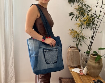 Może przedstawiać: Duża torba typu tote wykonana z recyklingowanego denimu z czerwoną i białą paskowaną podszewką. Torba ma dużą kieszeń z przodu i jest trzymana przez osobę w brązowym bezrękawniku.