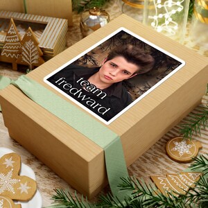May include: A brown gift box with a green ribbon and a sticker featuring a photo of a young man with the text "team edward".