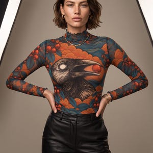 Peut inclure: Un haut à manches longues et col montant avec un imprimé graphique représentant un oiseau noir tenant une baie rouge dans son bec, sur un fond de motifs de vagues orange, de baies rouges et de feuilles bleues, porté avec un pantalon noir.