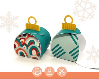 Op de afbeelding: Twee printbare kerstversiering cadeaudozen. Eén doos heeft een teal blauwe achtergrond met een rood, wit en blauw geometrisch patroon. De andere doos heeft een teal blauwe achtergrond met een wit en teal blauw gestreept patroon. Beide dozen hebben een gele ornament topper.