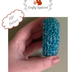 May include: A teal and white knitted wrist cuff, held in a hand. The cuff is made with a textured stitch pattern. The image includes the text "PDF Pattern".
