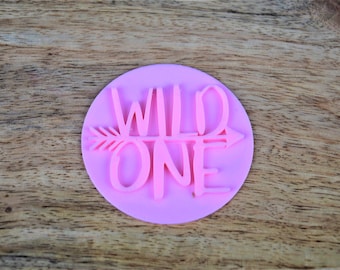 Może przedstawiać: Różowa silikonowa foremka do ciasta z napisem "WILD ONE" i wzorem strzałki.