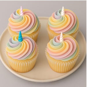 Peut inclure: Quatre petits gâteaux avec un glaçage arc-en-ciel pastel et une corne de licorne sur le dessus, disposés sur une assiette de couleur claire. Les tourbillons de glaçage sont dans des tons de rose, jaune, vert et violet.