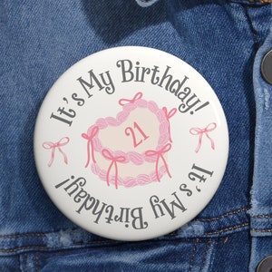May include: White button with the text "It's My Birthday!" and "It's My Birthday!" in a circle around a pink heart-shaped cake with the number 21 on it.