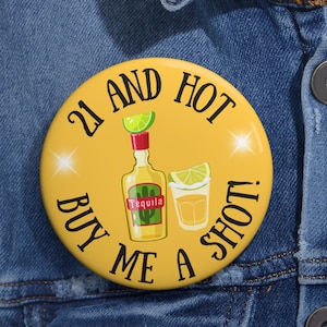 May include: A yellow button with the text "21 and hot buy me a shot!" in black. The button features a cartoon image of a bottle of tequila and a shot glass with a lime wedge.