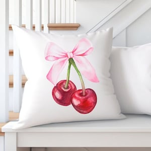 May include: White throw pillow with a pink bow and two red cherries on a white bench.