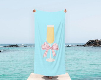 May include: A light blue beach towel with a pink bow and a glass of champagne on it.