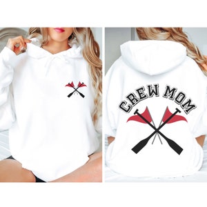 Puede incluir: Sudadera con capucha blanca con el texto "CREW MOM" en letras negras y grises con un diseño de remo rojo y gris en la parte posterior. La parte delantera de la sudadera tiene una versión más pequeña del diseño de remo.