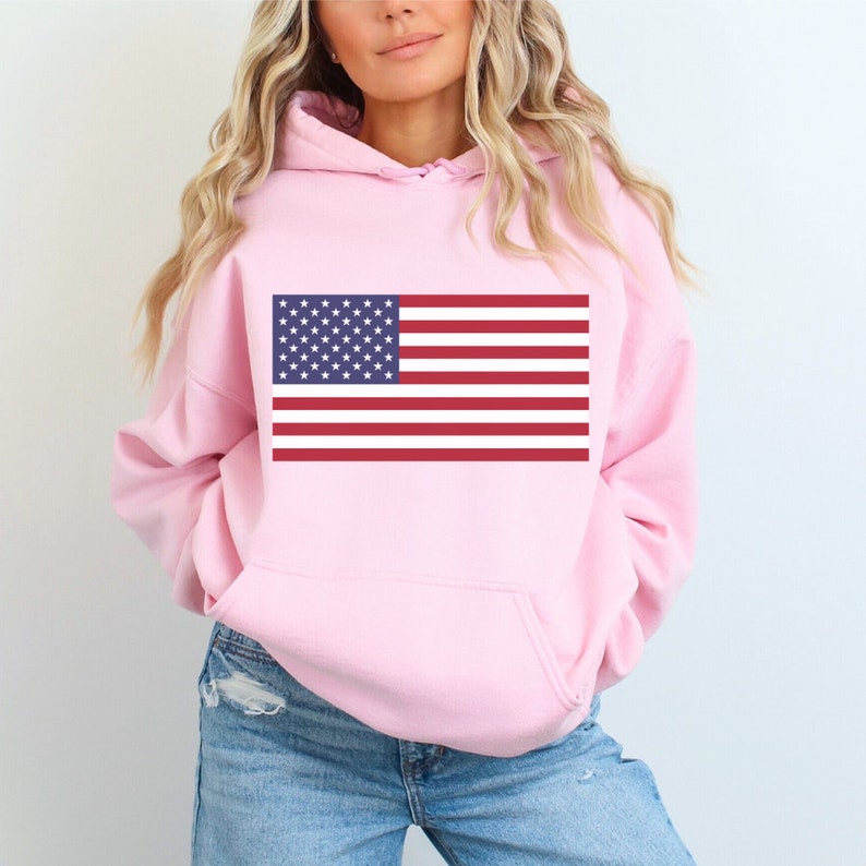 May include: A pink hoodie with a graphic of the American flag on the front. The hoodie has a drawstring hood and a kangaroo pocket.
