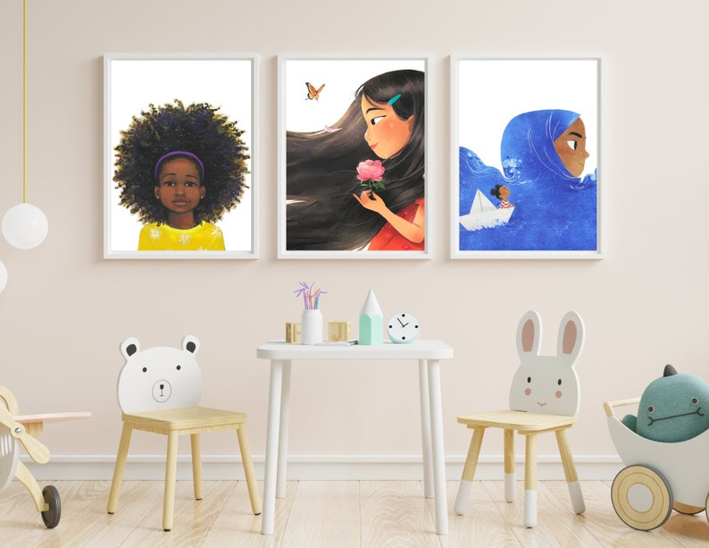 May include: Three framed illustrations of young girls. The first illustration features a young Black girl with curly hair wearing a yellow shirt. The second illustration features a young girl with long brown hair wearing a red dress. The third illustration features a young girl wearing a blue headscarf and a white dress. The illustrations are displayed on a white wall.