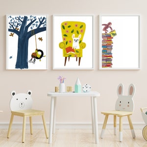 Op de afbeelding: Drie ingelijste illustraties op een witte muur. De illustraties tonen een boom met een schommel, een hond die in een gele fauteuil zit en een aap die op een stapel boeken klimt. De illustraties zijn in een kinderstijl met felle kleuren en eenvoudige vormen.