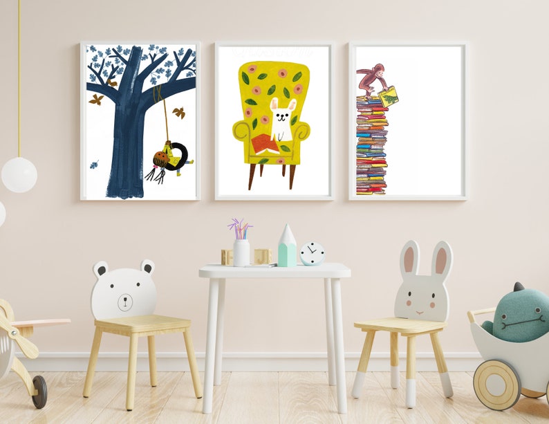 Op de afbeelding: Drie ingelijste illustraties op een witte muur. De illustraties tonen een boom met een schommel, een hond die in een gele fauteuil zit en een aap die op een stapel boeken klimt. De illustraties zijn in een kinderstijl met felle kleuren en eenvoudige vormen.