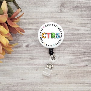 May include: White round badge with a black retractable badge reel. The badge has the text "CTRS" in colourful letters surrounded by the words "Remediate, Play, Rehabilitate, Restore" in a circle.