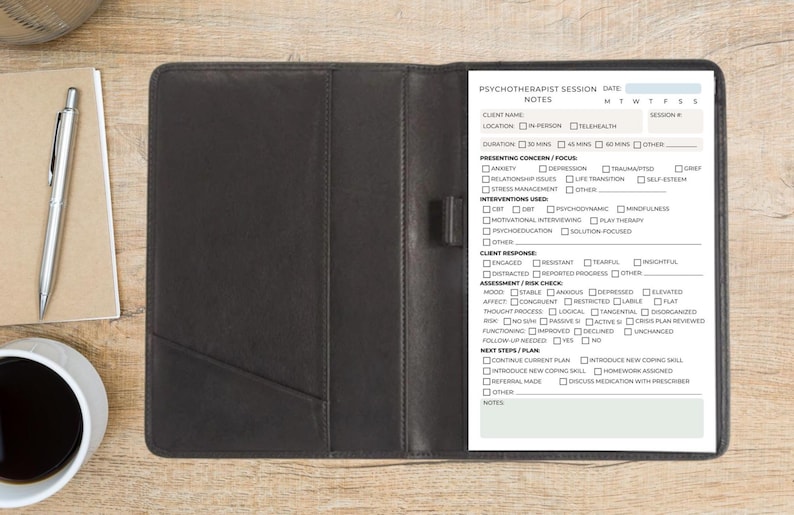 May include: A black leatherette portfolio with a notepad and pen, open to reveal a printed form labeled "Psychotherapist Session Notes." A cup of coffee and a notepad are on the wooden surface.
