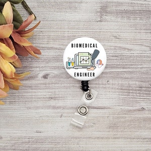 May include: White retractable badge holder with a round button featuring a colourful illustration of a laptop, test tubes, a stethoscope, and a prosthetic leg with the text "BIOMEDICAL ENGINEER".