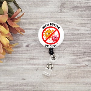 May include: A white retractable badge reel with the text "GERM BUSTER ON DUTY" in black. The design features a red circle with a line through it, containing cartoon germs. The reel is attached to a clear plastic strap.