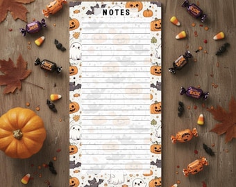 May include: A Halloween-themed notepad with the word "NOTES" at the top. The notepad is decorated with pumpkins, ghosts, and bats. Candy corn and wrapped candies surround the notepad on a wooden surface.