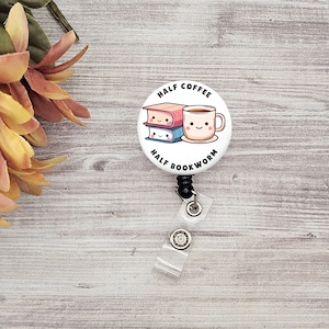 May include: A white badge reel with the text "HALF COFFEE HALF BOOKWORM" and a graphic of a coffee mug and two books. The reel has a black clip and a clear plastic strap. The background is a light wood grain.
