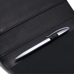 May include: A black leather portfolio with a silver pen. The pen has a black band near the top. The portfolio has several pockets and is open, revealing the interior. The pen is resting on the portfolio.
