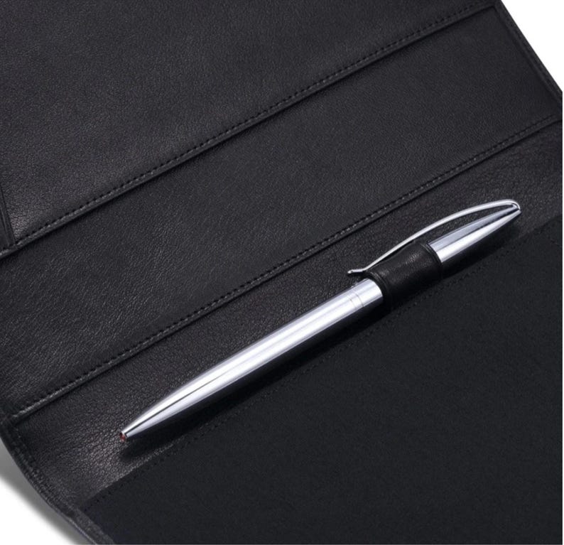 May include: A black leather portfolio with a silver pen. The pen has a black band near the top. The portfolio has several pockets and is open, revealing the interior. The pen is resting on the portfolio.