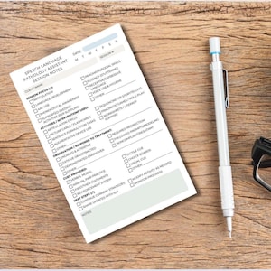 May include: A Speech Language Pathology Assistant session notes form with checkboxes and prompts, next to a mechanical pencil and eyeglasses on a wooden surface. The form includes sections for client information, session focus, activities, and observations.