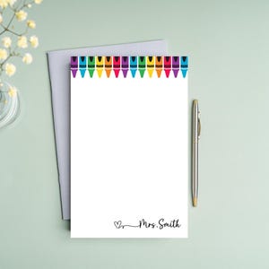 May include: White notepad with a border of colorful crayons at the top. The notepad has a line at the bottom with the text "Mrs. Smith" and a small heart.