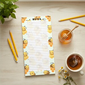 May include: A notepad with a light green background and lined pages. The notepad is decorated with cartoon bees and honeycomb patterns. The word "NOTES" is at the top. Also pictured are pencils, honey, and a cup of tea.