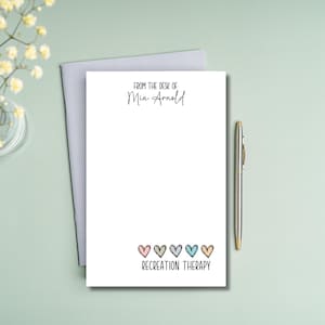 May include: A white notepad with the text "From the desk of Mia Arnold" and "Recreation Therapy" with a row of five colorful hearts at the bottom.