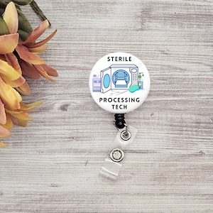 May include: White badge reel with a white button featuring a cartoon illustration of a sterilisation machine with the text "STERILE PROCESSING TECH".
