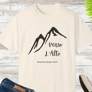 May include: A white t-shirt with a black mountain graphic and the text "Verso L'Alto" and "Blessed Pier Giorgio Frassati".