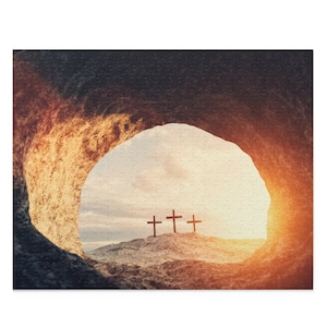 May include: A view from inside a cave looking out at three wooden crosses silhouetted against a bright, orange sunset. The crosses are on a rocky hilltop.