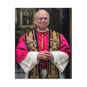 Puede incluir: Retrato de un hombre con vestiduras religiosas. Las vestiduras son principalmente de color magenta con detalles bordados en oro y marrón. El hombre lleva gafas y un anillo de oro. El fondo es un interior de iglesia.