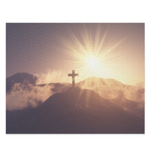 May include: A silhouette of a wooden cross on a mountaintop with a bright sun shining through clouds in the background.