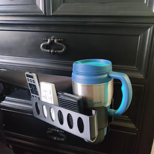 May include: A black plastic organizer with six slots for remotes, a phone, or other small items. A blue travel mug with a teal lid and the word "Bubba" on the side is in the organizer.