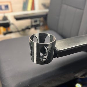 May include: A black and white striped cup holder attached to a black armrest. The cup holder has a round opening and is designed to hold a beverage.