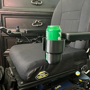 May include: A black wheelchair with a green can in a black cup holder. The wheelchair has a black seat and a blue frame. The wheelchair has a "Spectrum Foam SR" label on the seat.