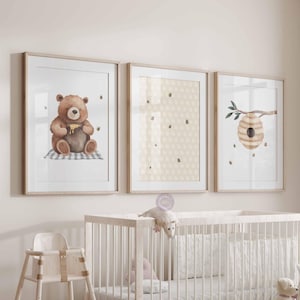 May include: Three framed prints with a watercolor illustration of a bear holding a honey pot, a honeycomb pattern, and a beehive with a branch. The prints are hung on a white wall above a white crib.