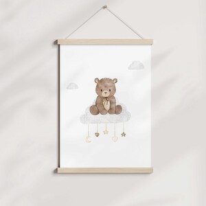 May include: A brown teddy bear sitting on a white cloud with gold stars and hearts hanging from it. The background is white.