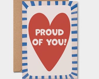 May include: A white card with a red heart and blue and white stripes around the edges. The heart has the text "PROUD OF YOU!" in white.
