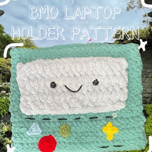 Op de afbeelding: Een gehaakte laptopstandaard in de vorm van het personage BMO uit de cartoon Adventure Time. De standaard is groen met een wit scherm en een glimlachend gezicht. Hij heeft een ontwerp met rode, gele en groene knoppen.