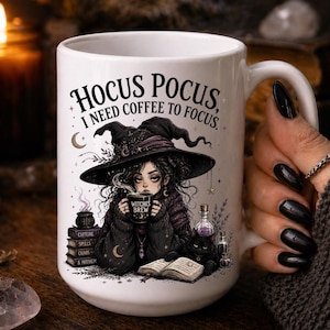 May include: White ceramic mug with a witch illustration and the text "Hocus Pocus, I need coffee to focus." The witch is wearing a hat and holding a mug that says "Witches Brew". A black cat and books are also featured.