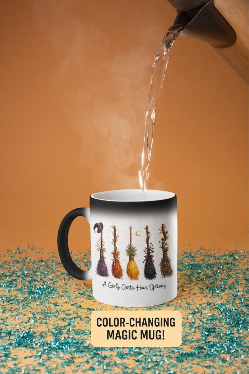Puede incluir: Una taza m&aacute;gica que cambia de color con asa y borde negros. La taza blanca presenta un dise&ntilde;o de seis coloridas escobas de bruja y el texto "A Girl's Gotta Have Options". Se vierte agua en la taza.