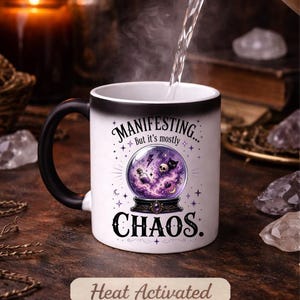May include: White heat-activated mug with a black handle. The mug features the text "MANIFESTING... but it's mostly CHAOS" with a crystal ball graphic. The words "Heat Activated" are also printed on the mug.