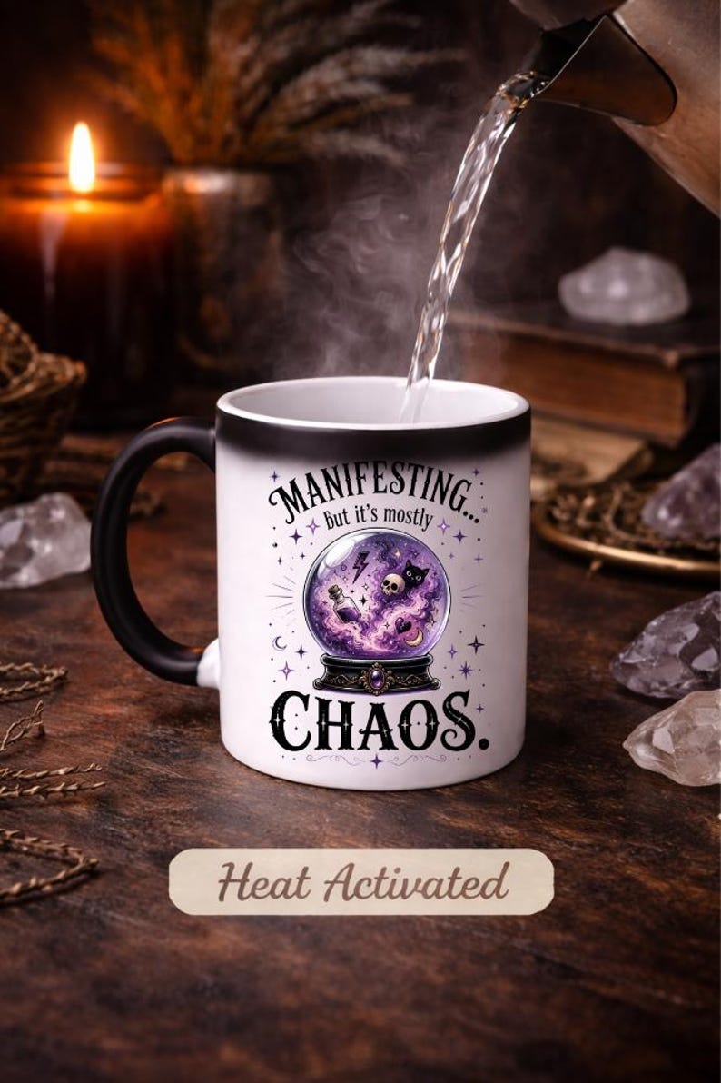 May include: White heat-activated mug with a black handle. The mug features the text "MANIFESTING... but it's mostly CHAOS" with a crystal ball graphic. The words "Heat Activated" are also printed on the mug.